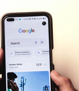 A close-up of a hand holding a smartphone with Google search displayed on the screen.