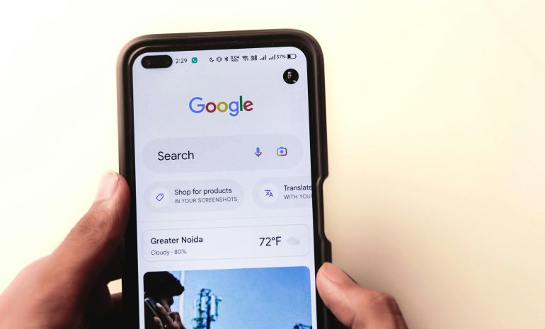 A close-up of a hand holding a smartphone with Google search displayed on the screen.