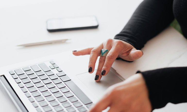 A businesswoman's hands typing on a laptop at a bright, modern workspace.