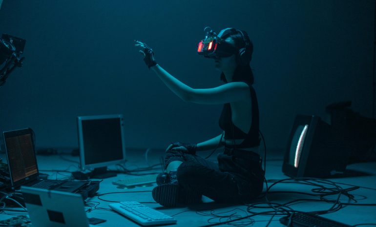 Woman immersed in virtual reality, surrounded by tech, in a dimly lit room.